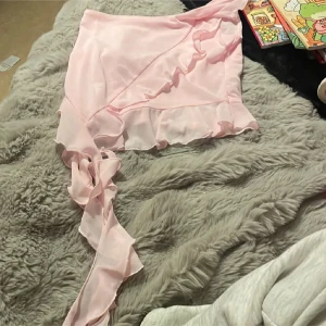 Ljusrosa omlotttopp med volang - Supersöt ljusrosa omlotttopp med volangkant  toppen har en flowy känsla och är gjord i ett tunt, lätt material som ger en romantisk vibe. Perfekt för dig som gillar en feminin och trendig stil.