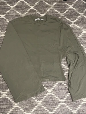 Olivgrön långärmad tröja 157 XS - Olivgrön långärmad tröja från 157 i storlek XS. Tröjan har en enkel och clean design med rund hals och raka ärmar. Tillverkad i mjuk bomull som är skön mot huden. Perfekt för dig som gillar minimalistisk stil och vill ha en basic topp i garderoben.