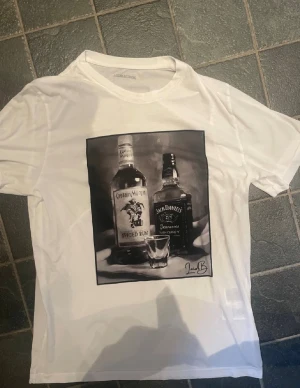 Vit t shirt  - Vit t-shirt med svartvitt tryck av Captain Morgan och Jack Daniel's flaskor samt ett shotglas. T-shirten är från Laidbclothing, storlek M.