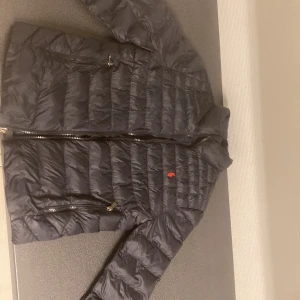 Svart dunjacka från Polo Ralph Lauren - Svart dunjacka från Polo Ralph Lauren med quiltad design och två dragkedjeförsedda  Perfekt för kalla dagar och har en stilren look som funkar till det mesta. Den har en liten hål vid ena sidan. Passar 160-165 cm