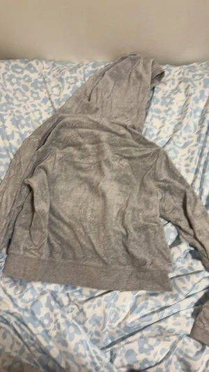 Grå hoodie Juicy Couture L - Mjuk och chill grå hoodie från Juicy Couture i storlek L. Tröjan har dragkedja, snörning i huvan och långa ärmar. Materialet är skönt och känns lite som velour. Perfekt för att hänga hemma eller dra på sig när det är lite kyligt.