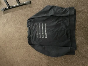 Svart Peak Performance sweatshirt 160 - Svart sweatshirt från Peak Performance med tryckt logga i vitt och grått på bröstet. Tröjan har rund hals, ribbade muddar vid ärmslut och nederkant samt lång ärm. Perfekt för dig som gillar stilren och enkel design.