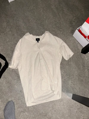 Beige kortärmad skjorta H&M linne - Kortärmad beige skjorta från H&M i regular fit. Skjortan har knappar framtill, bröstficka och är tillverkad i ett luftigt linnematerial. Perfekt för varma dagar och enkel att styla med jeans eller shorts. Använd typ 2 gånger