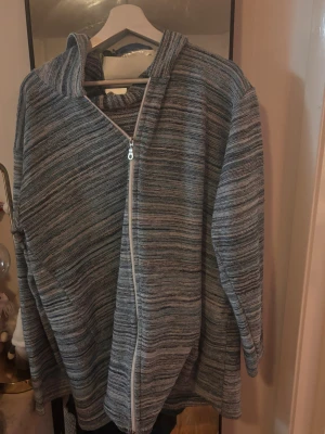 Randig stickad jacka med dragkedja - Mysig tjocktröja i  blått med randigt mönster och  dragkedja framtill. Tröjan har  lång ärm, 