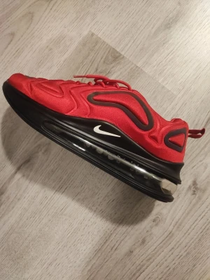Nike Air Max 720 röda sneakers - Nike Air Max 720 sneakers i rött med svarta och mörkgrå detaljer. Skorna har en futuristisk design med vågiga mönster, stor synlig Air Max-sula och snörning. Ovandelen är i syntetmaterial och mesh för extra komfort. Snygg och sportig look med tydlig 720-märkning bak.