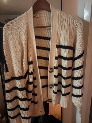 Randig kofta från JDY i XL - Snygg stickad kofta från JDY i storlek XL. Koftan är vit med svarta horisontella ränder, har långa ärmar och tre stora knappar 