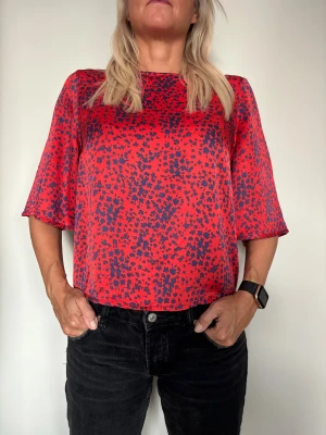 Röd blommig blus från Rodebjer - Säljer Rodebjers klassiska top Cadea med mörkblått blommönster i 100% viskos. Storlek S. Skick - inget att anmärka på. 600kr. Modellen har rund hals, halvlånga vida ärmar och knapp i nacken. Tillverkad i mjuk viskos som ger ett snyggt fall. Perfekt för dig som vill ha en färgstark och unik topp.