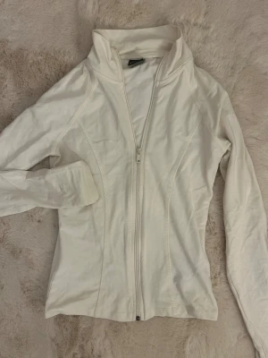 Vit långärmad ziptröja från Gina Tricot - Säljer en vit långärmad ziptröja från Gina Tricot i storlek XS. Tröjan har en hög krage och hel dragkedja framtill. Materialet är mjukt och skönt bomull, perfekt för chill dagar eller när du vill ha en clean look.