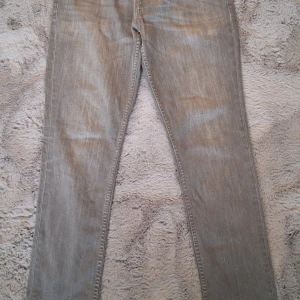 Levis grå jeans W30 L30 - Snygga grå Levis jeans med klassisk femficksdesign och röd Levis-tag på bakfickan. Jeansen har rak passform och är tillverkade i mjukt jeanstyg med diskret slitning för en cool look. Perfekta för dig som gillar stilrena och tidlösa jeans. Osäker på modell då lappen baktill är borta, ev 501. 