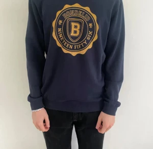 Mörkblå tröja - Säljer en snygg mörkblå tröja från Bondelid med ett stort tryck på framsidan. Passform S-M. Modellen på bilden är cirka 180 och väger cirka 70 kg.