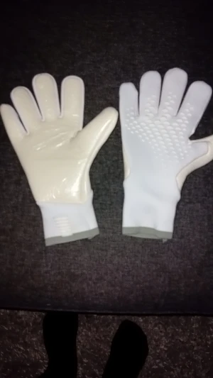 Vita målvaktshandskar med grepp - Säljer ett par vita målvaktshandskar med grå kant vid handleden. Handflatan är slät och glansig medan ovansidan har mönstrade greppzoner för bättre bollkontroll. Handskarna har en sportig look och är perfekta för fotbollsträning eller match. Helt nya med plast.