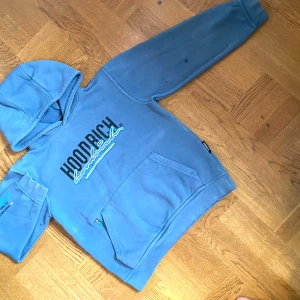 Blå hoodie från Hoodrich med tryck - (SVARTA FLÄCKEN PÅ ARMEN OCH TRÖJAN ÄR BARA VATTEN!)     Snygg blå hoodie från Hoodrich med svart och turkost tryck på bröstet och ärmen. Tröjan har huva, känguruficka med dragkedja och lång ärm. Perfekt för dig som gillar streetwear och vill ha en cool look.