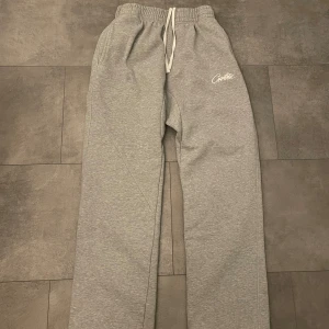 Grå mjukisbyxor från Corteiz, medium - Grå mjukisbyxor från Corteiz i storlek medium. Byxorna har resår och snörning i midjan, broderad logga på vänster ben och är tillverkade i mjukt bomullsmaterial. Perfekta för chill dagar och har en klassisk loose passform.