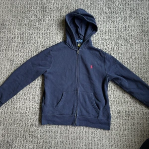 Mörkblå zip hoodie Ralph Lauren - Säljer en mörkblå hoodie från Ralph Lauren i storlek 14-16. Den passar om man är ca 160-170 lång. Den är i bra skick. Priset är förhandlingsbart.