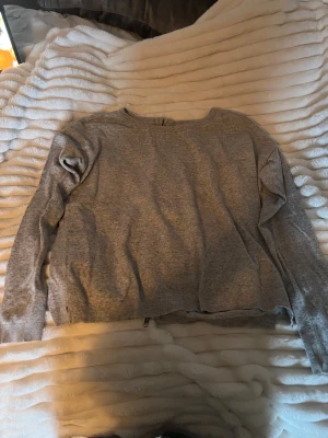 Grå tröja med dragkedja i bak från mbyM - Gråmelerad tröja från mbyM i storlek S/M. Tröjan har lång ärm, rund halsringning och en snygg dragkedja längs hela ryggen. Tillverkad i mjuk bomullsblandning, perfekt för lager-på-lager under höst och vår.