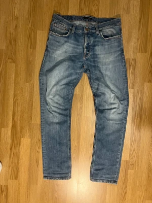Nudie jeans -2012 - Snygga blå jeans från Nudie Jeans med klassisk femficksdesign och orangea sömmar. Jeansen har en straight passform och är tillverkade i slitstarkt denim med Nudie-logga på bakfickan. Inköpta år 2012 och har fått sköna slitningar med tiden, W-33 L-32, vid minsta fråga hör av dig 