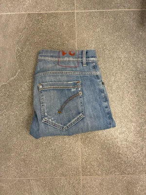 Dondup George ljusblå jeans, storlek 31 - Säljer ett par klassiska dondup jeans i ljusblå tvätt med snygga slitningar och raka ben. Jeansen har fem fickor, knappgylf och coola detaljer på bakfickorna. Perfekt för dig som gillar en tidlös och avslappnad stil.