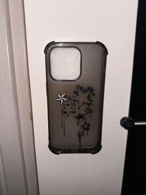 mobilskal till iphone 14 pro - Ett mobilskal till en iphone 14 pro. I genomskinlig/svart färg. Med mönster som är sjärnor. Mobilskalet är från shein.