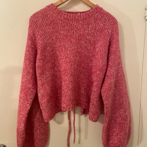 Rosa stickad tröja med öppen rygg NA-KD - Superfin rosa stickad tröja från NA-KD med ballongärmar och cool öppen rygg med snörning. Använd fåtal gånger. När jag skulle ta bilderna såg jag att vänstra ärmen fått en liten, liten fläck men knappast något som syns i verkligheten!🥰