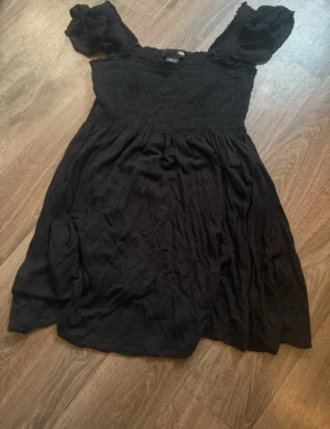 Svart linne från H&M Str XS - Supersöt svart linne från H&M i storlek XS. Linnet har smockad överdel, puffiga korta ärmar och en flowy nederdel. Super snygg💕