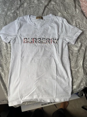 Vit Burberry t-shirt med logga - Vit t-shirt från Burberry med broderad logga i rött, svart och beige på bröstet. Klassisk rund halsringning och korta ärmar. Tillverkad i mjuk bomull för en skön känsla och clean look.