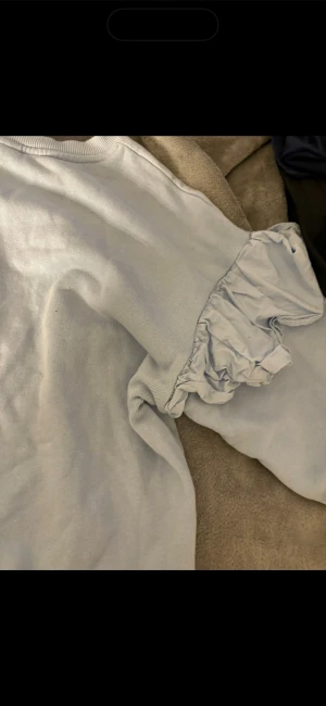 Ljusblå stickad tröja med volangärm - Supersöt ljusblå stickad tröja med rund hals och unika volangdetaljer på ärmarna. Perfekt för dig som gillar en enkel men ändå lekfull stil. Materialet är mjukt och skönt, och färgen är fräsch och passar till mycket. Passar upp till storlek L.