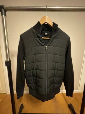 Svart quiltad pufferjacka från Next - Svart pufferjacka från Next med quiltad front och mjuka ärmar. Jackan har dragkedja hela vägen och ribbade muddar vid ärmslut och nederkant. Perfekt för dig som gillar stilren och enkel design med lite edge.