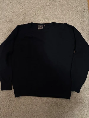 Svart stickad tröja Oscar Jacobson - Svart stickad tröja från Oscar Jacobson, tillverkad i Italien. Klassisk rund hals och långärmad modell, perfekt för dig som gillar stilrena och enkla plagg. Materialet är mjukt och skönt, passar dig som vill ha en basic tröja med premiumkänsla. Har några små hål som inte syns 