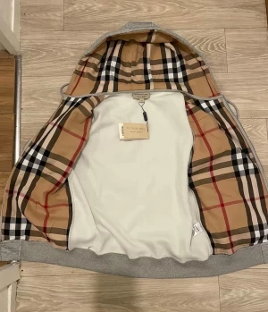 Grå hoodiejacka från Burberry - Grå hoodiejacka från Burberry med klassiskt rutigt foder i huvan och insidan. Jackan har dragkedja framtill, snörning i huvan och broderad Burberry-logga på bröstet. Tillverkad i mjuk bomullsmix för en chill och snygg look.