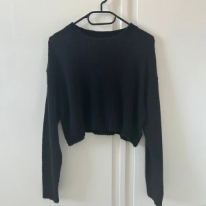 Svart croppad stickad tröja - En svart tunn croppad stickad tröja med rund halsringning och långa ärmar. Tröjan har ribbade muddar vid ärmslut och nederkant, vilket ger en snygg och enkel look. Perfekt att styla med höga jeans eller kjol.