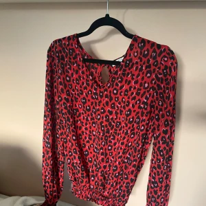 Röd leopardmönstrad blus från Pieces - Säljer en röd blus från Pieces med leopardmönster i svart och rosa. Blusen har långa ärmar, resår i midjan och en liten öppning med knapp i nacken. Perfekt statement-plagg för dig som gillar att sticka ut. Sjukt snygg❤️❤️