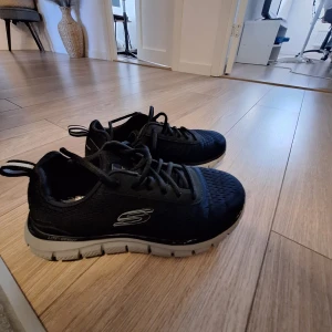 Svarta Skechers sneakers stl 40 - Svarta blåa  Skechers sneakers med grå sula och snörning. Ovandelen är i textil och syntetmaterial, med Skechers-logga på sidan. Skorna har rund tå och platt sula, perfekta för en aktiv vardag.  Inlägg till skorna saknas går att köpa där av 300 priset kostade 700 som nypris . Är I bra skick använda fåtal gånger .