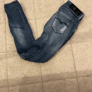 Replay jeans  - Säljer ett par blå skinny jeans från Replay med snygga slitningar och ljusa partier framtill. Klassisk femficksmodell med normal midja och smal passform. Jeansen har tydliga Replay-detaljer på bakfickan och är tillverkade i stretchigt jeansmaterial.
