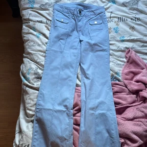 Ljusblå bootcut byxor från H&M Divided  - Snygga ljusblå bootcut byxor från H&M Divided med två fickor framtill med lock och silvriga knappar. Byxorna har låg midja och är gjorda i bomullsmix som känns mjuk och skön. Perfekta för en trendig och avslappnad look. Bara använt en gång. 