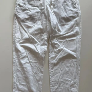 Vita linnebyxor med snörning - Snygga vita linnebyxor med avslappnad passform och snörning i midjan. Perfekta för varma dagar och ger en fräsch och stilren look. Byxorna har sidofickor och är tillverkade i ett lätt och luftigt material.