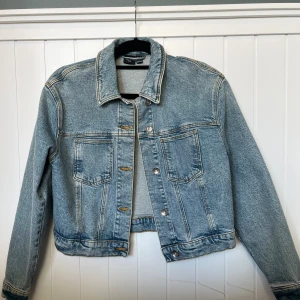 Ljusblå jeansjacka från Vero Moda - Säljer en klassisk ljusblå jeansjacka från Vero Moda. Jackan har två bröstfickor med lock, knappar framtill och en rak passform. Perfekt att slänga över en hoodie eller t-shirt för en chill look. Långärmad och i mjukt denimtyg.