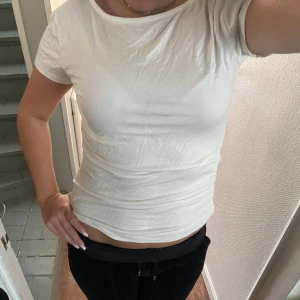Vit topp med öppen rygg och knyt - Säljer en vit topp med korta ärmar och snygg öppen rygg med knytband. storlek m men sitter som xs/s. Toppen är figurnära och har en enkel, stilren look framtill medan ryggen har en cool detalj med rosett. Perfekt för dig som gillar trendiga plagg