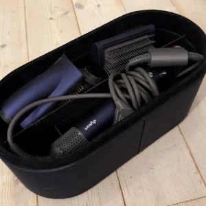 Svart sminkväska från Dyson - Snygg oval sminkväska i svart från Dyson, perfekt för att förvara dina sminkborstar och andra sminkverktyg. Väskan har flera fack och är tillverkad i ett slitstarkt material med stilren design. Passar dig som vill ha ordning på sminket och gillar modern look.