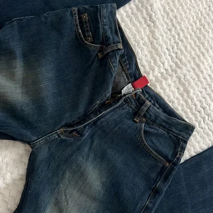 Mörkblå lowwaist jeans från Tipster - Snygga mörkblå lowwaist jeans från Tipster med klassisk femficksdesign och kontrastsömmar. Jeansen har utsvängda ben och subtila slitningar framtill för en cool look. Tillverkade i robust denim som passar perfekt till vardagsstilen.