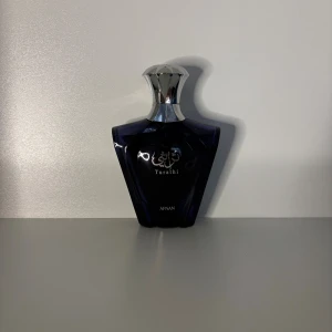 Afnan Turathi sampel - Afnan Turathi parfym i en snygg mörkblå glasflaska med silverfärgad metallkork. Flaskan har en elegant, modern form och text i både arabiska och engelska på framsidan. Perfekt för dig som gillar exklusiva dofter och stilren design.