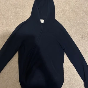 Mörkblå hoodie i kashmir från John Henric - Exklusiv mörkblå hoodie från John Henric i 100% kashmir. Tröjan har huva, lång ärm och en klassisk känguruficka framtill. Perfekt för dig som vill ha en mjuk och lyxig känsla i vardagen. Enkel och stilren design som funkar till allt.