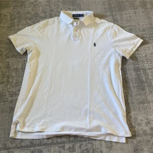Vit Polo Ralph Lauren t-shirt slim fit - Kommer med dustpåse!!!!!!!! Vit t-shirt från Polo Ralph Lauren med klassisk krage och korta ärmar. Custom slim fit-modell i mjuk bomull, med den ikoniska lilla logon broderad på bröstet. Perfekt för dig som gillar stilrena och tidlösa plagg.