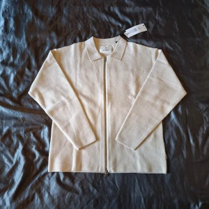 Beige kofta med dragkedja Jack & Jones - Stilren beige kofta från Jack & Jones med hel dragkedja framtill och klassisk krage. Tillverkad i en mjuk blandning av material som ger en skön känsla. Perfekt för lager-på-lager och enkel att matcha med andra plagg.