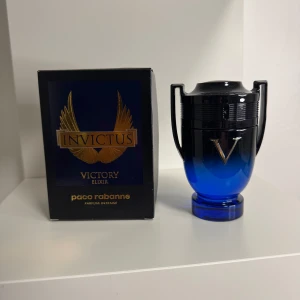 Paco Rabanne Invictus Victory Elixir - Parfymen Invictus Victory Elixir från Paco Rabanne kommer i en cool blå och svart troféformad flaska med silverdetaljer. Doften är intensiv och exklusiv, perfekt för dig som vill sticka ut. Förpackningen är svart med guldiga vingar och text.
