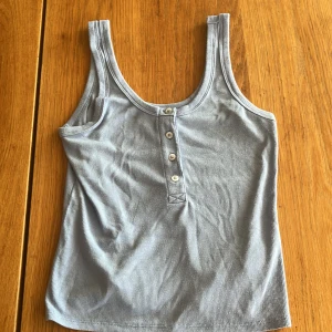 Ljusblå ribbad linnetopp från ONLY - Säljer en ljusblå ribbad linnetopp från ONLY i storlek XS. Toppen har knappar framtill och är ärmlös med klassisk rund halsringning. Perfekt för varma dagar och enkel att matcha med jeans eller shorts.