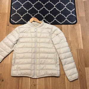 Beige pufferjacka från Womenswear - Lätt och stilren beige pufferjacka från Womenswear, grundat i Köpenhamn. Jackan har quiltad design, lång ärm och dragkedja framtill. Perfekt för kyliga dagar och enkel att matcha med olika outfits. Därmed så är jag en S och en Xs person så den passar för båda.