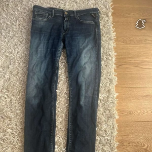 Mörkblå Replay jeans straight fit - Snygga mörkblå jeans från Replay med klassisk femficksdesign och raka ben. Jeansen har diskreta slitningar framtill och coola detaljer på bakfickorna. Perfekta för dig som gillar en tidlös och avslappnad stil.