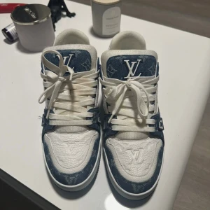 Louis Vuitton Trainer Sneakers - Snygga Louis Vuitton sneakers i blått och vitt med klassiskt LV-monogram på denim och detaljer i vitt skinn. Skorna har rund tå, platt sula och vita snören. Perfekta för dig som vill sticka ut med exklusiv streetstyle.