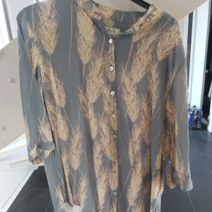 Blåbeige skjirta med naturmönster - Säljer en skjorta med blå botten och beige naturinspirerat mönster. Skjortan har knappar hela vägen framtill och trekvartsärmar. 