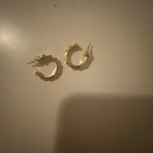 Guldiga örhängen med kantig design - Säljer ett par små, guldiga hoops med cool kantig och geometrisk form. 